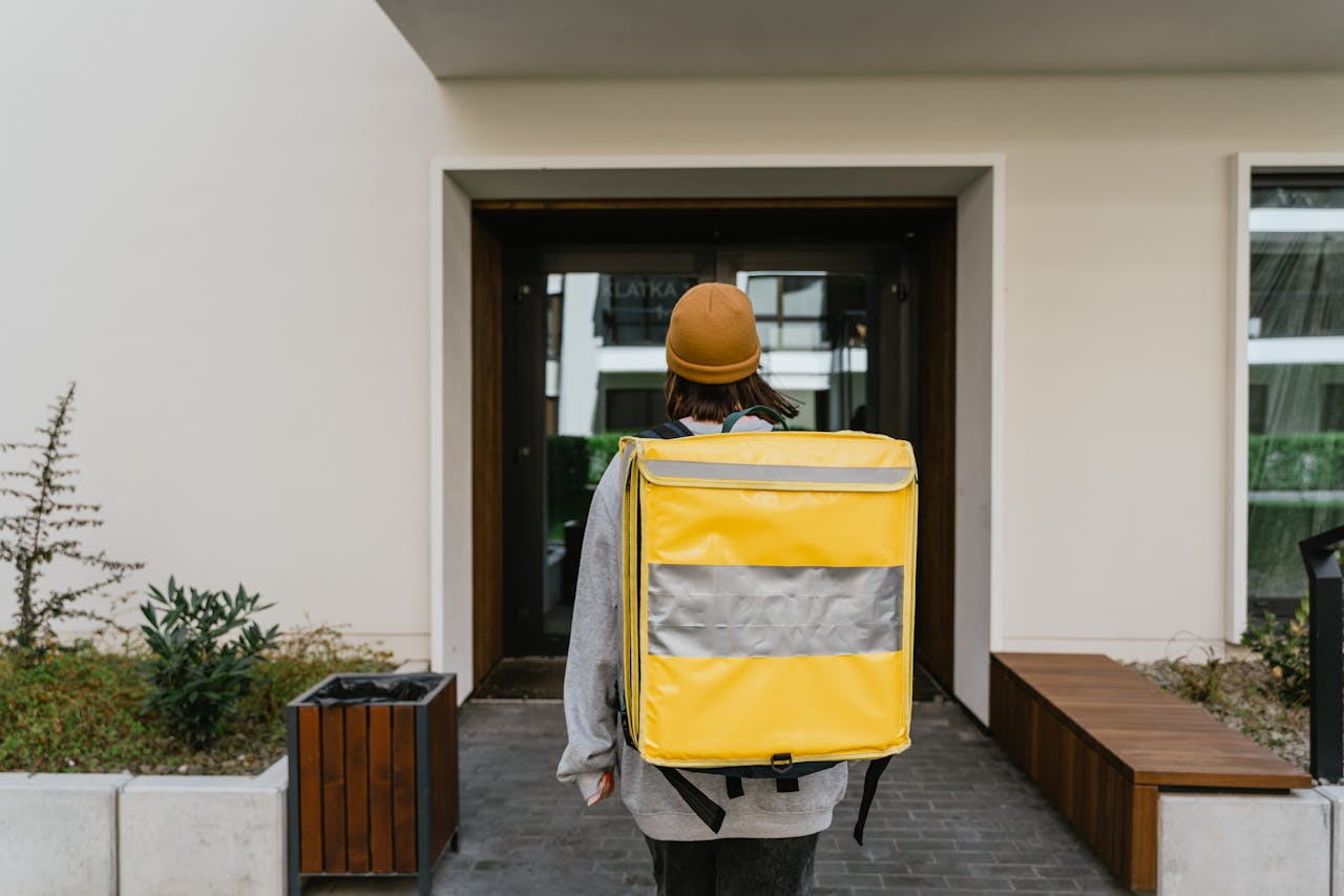 why-choose-us-02 A food delivery person with a yellow thermal backpack entering a modern building.
